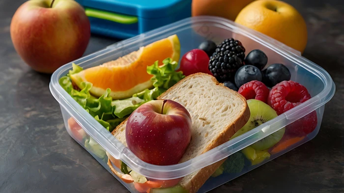 Ilustrasi kotak bekal sekolah berisi buah-buahan segar, sandwich gandum, dan sayuran sebagai pola makan sehat anak.