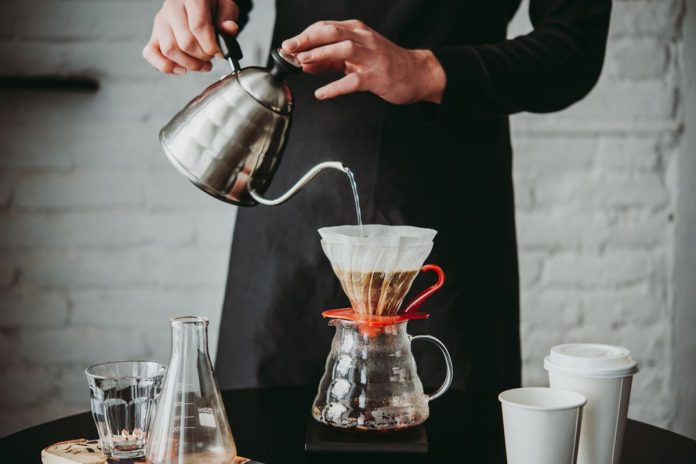 Seseorang sedang menyeduh kopi di rumah menggunakan metode manual brew untuk menghemat pengeluaran harian.