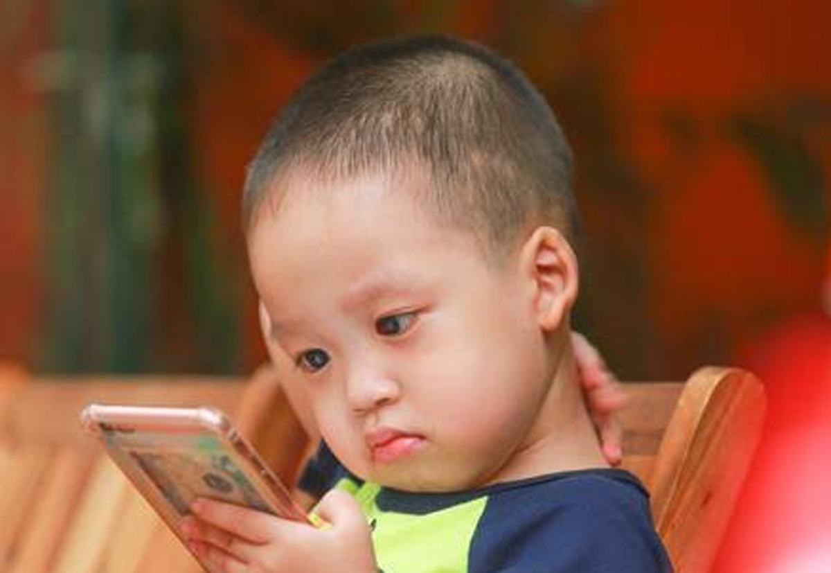 Ilustrasi seorang anak yang terlalu fokus menatap layar gadget di ruangan gelap, menggambarkan risiko paparan cahaya biru dan gangguan postur tubuh.